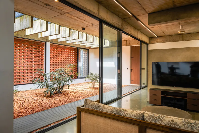 Living room overlooking the internal courtyard through floor-to-ceiling glazing with exposed concrete ceiling above