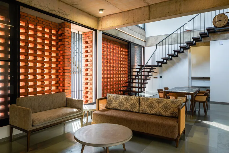 Double-height living space with spiral staircase, perforated brick wall and exposed concrete structure in daylight
