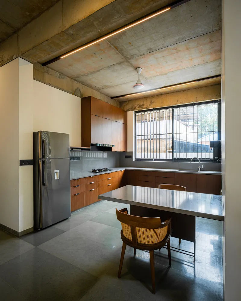 Kitchen with wood cabinetry and exposed concrete ceiling beams lit by recessed linear strips