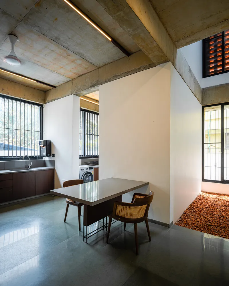 Dining area with freestanding white wall beneath exposed concrete ceiling and linear lighting