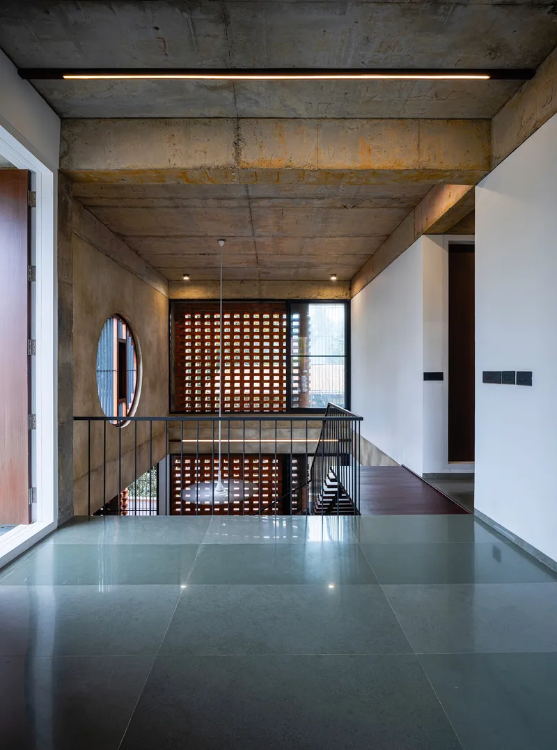 Upper landing with perforated terracotta screen and metal railing under board-formed concrete ceiling