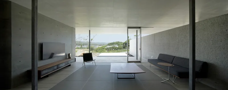 Living space with concrete walls and dark tile floor opening to landscape views through sliding glass