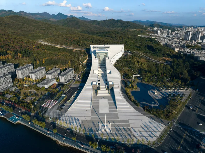 Aerial view of the white terraced structure with forested hills and residential blocks in the background