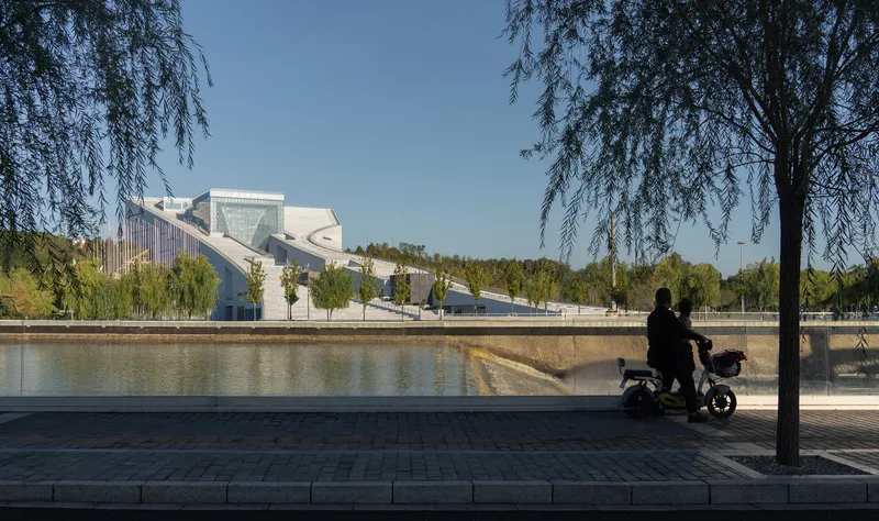 View across the canal showing the white facade and ramped form framed by willow trees