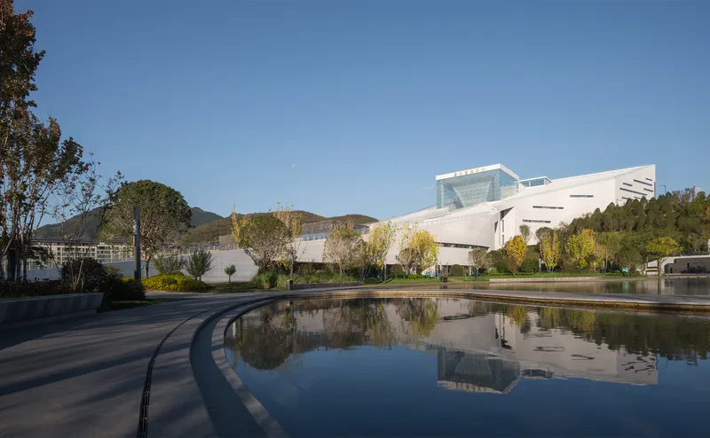 Curved reflecting pool mirroring the white cantilevered volume and surrounding hillside under clear sky