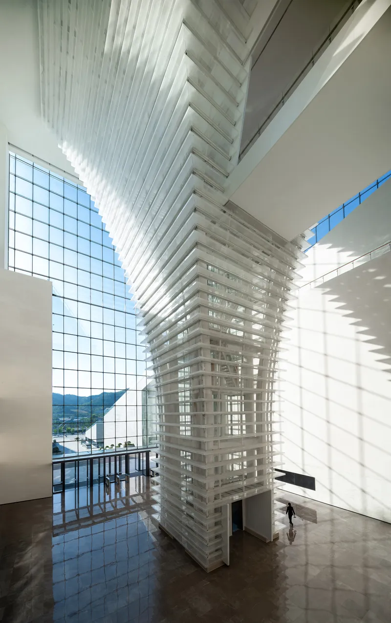 Interior atrium with layered horizontal fins and curtain wall framing a single visitor below