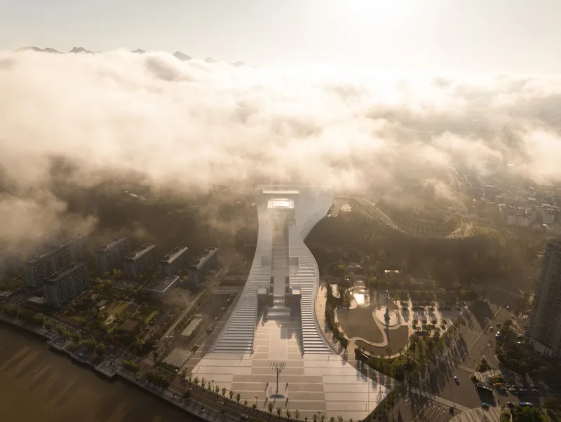Aerial view of the axial stepped plaza and monumental stairway emerging from morning fog