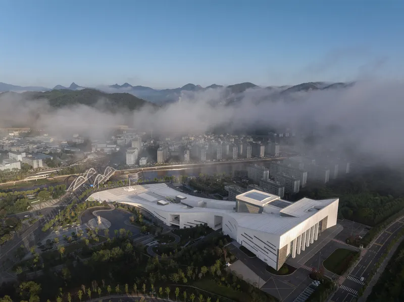 Drone view of the complex with curving bridge and surrounding town shrouded in morning fog