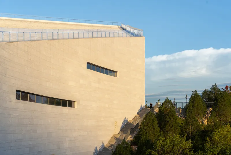 Pale stone facade with horizontal ribbon windows and rooftop railing under late afternoon light