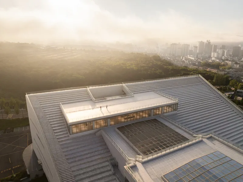 Aerial view of the stepped metal roof terraces with skylights overlooking a hazy valley