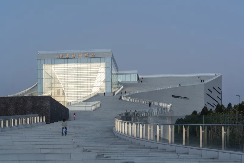 Wide stone staircase rising toward the illuminated glass volume with visitors on the steps
