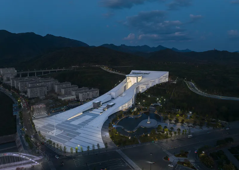 Drone view of the terraced roof complex beside a landscaped park at twilight with mountains beyond