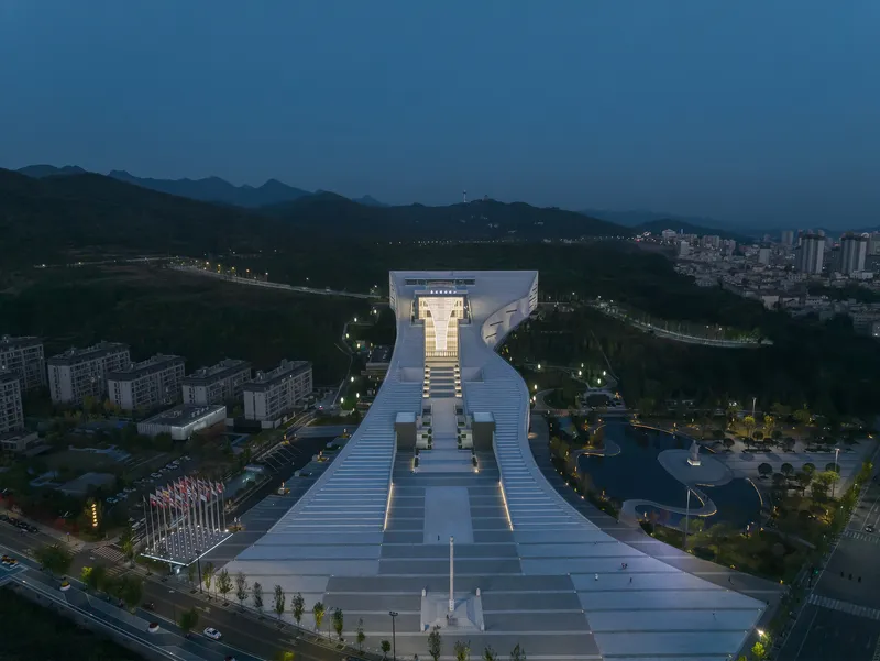 Elevated view of the stepped plaza leading to the elevated pavilion volume at dusk