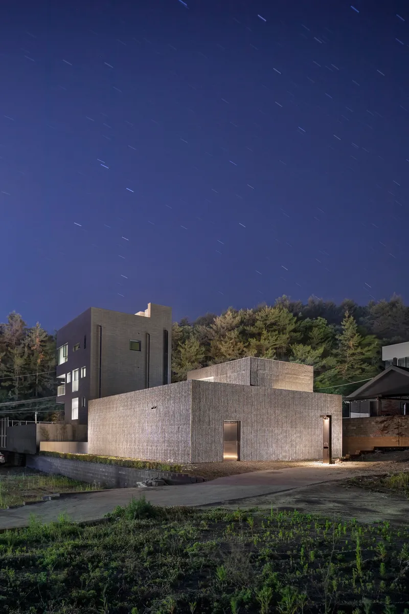Textured concrete volumes with corner windows photographed under star trails at twilight