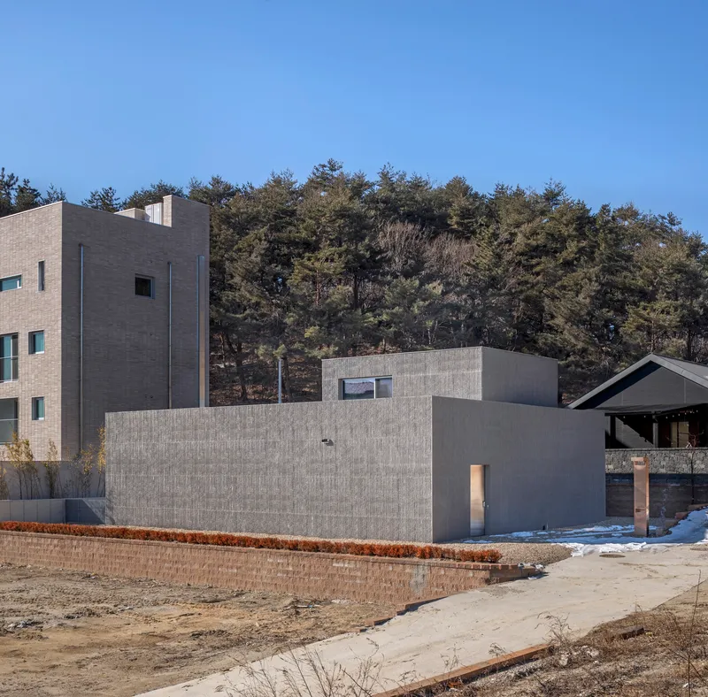 Concrete block volumes with board-formed wall against a forested hillside in late winter light