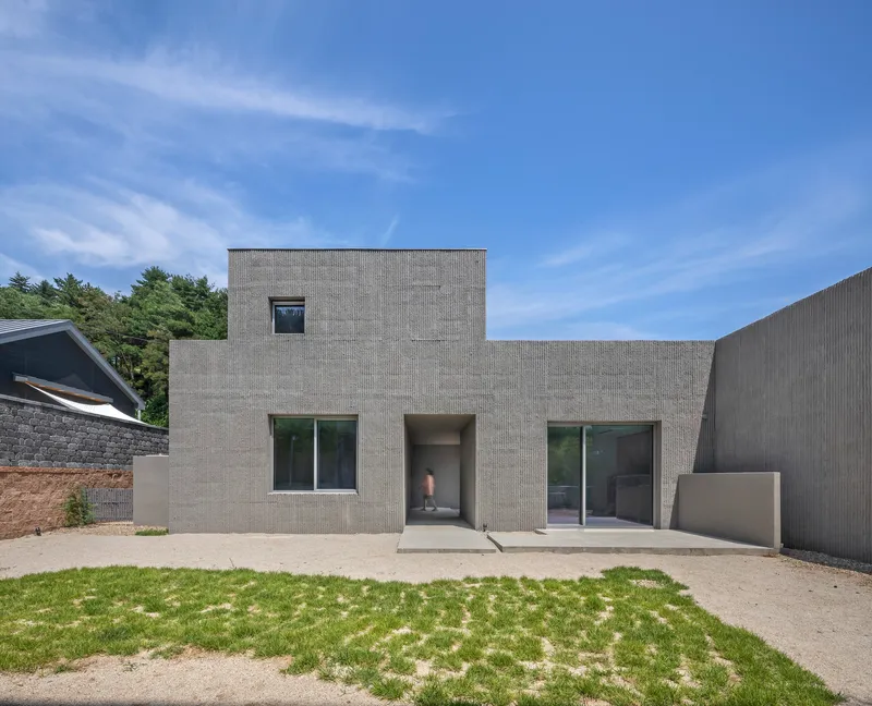 Front facade of concrete block residence with recessed entry and grass courtyard under clear skies