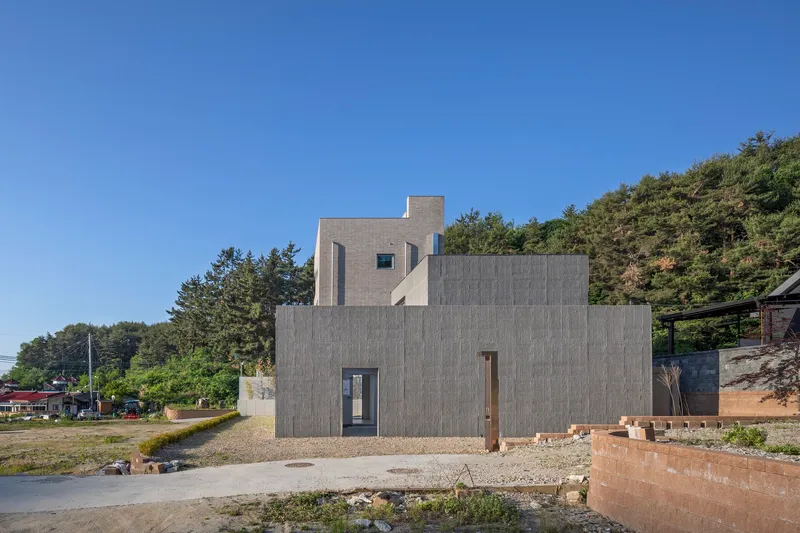 Stacked concrete block volumes with narrow windows set into a hillside along a gravel drive