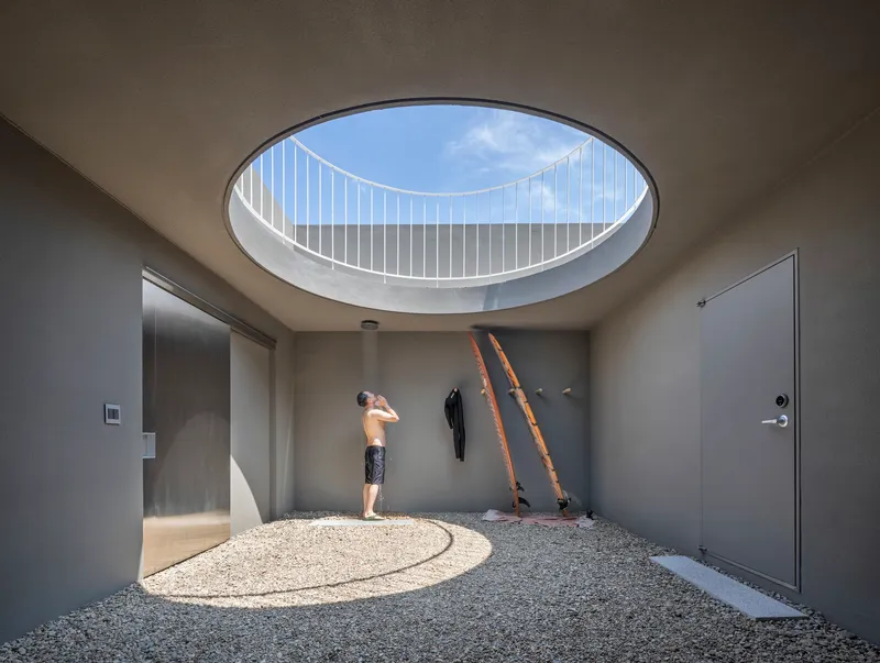 Entry hall with circular skylight above a gravel floor where a child stands in afternoon sun
