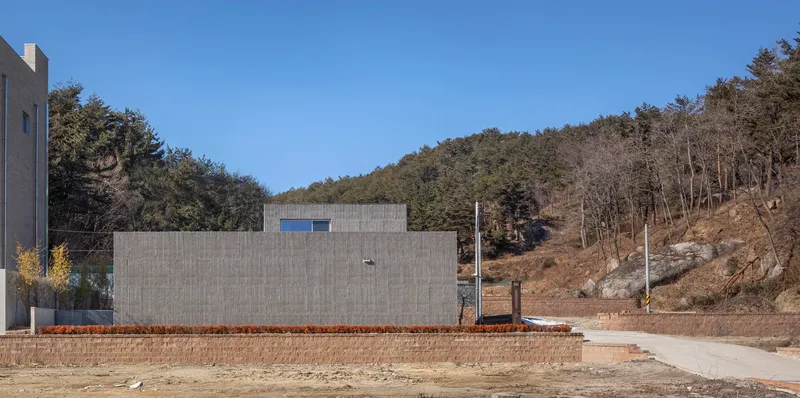 Rear elevation of the concrete block wall facing a hillside road during winter or early spring