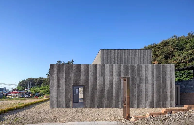 Corrugated metal facade with stepped volumes and a central glazed entry on gravel ground