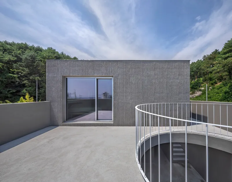 Rooftop terrace with curved metal railing and sliding glass doors against ribbed cladding