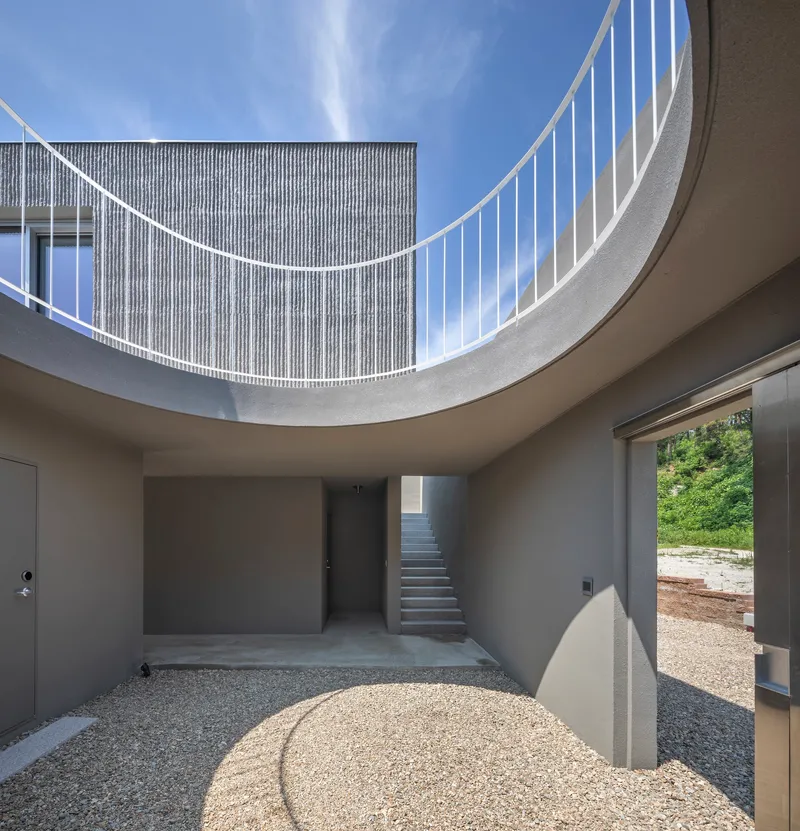 Circular courtyard open to sky with curved railing above and gravel floor below