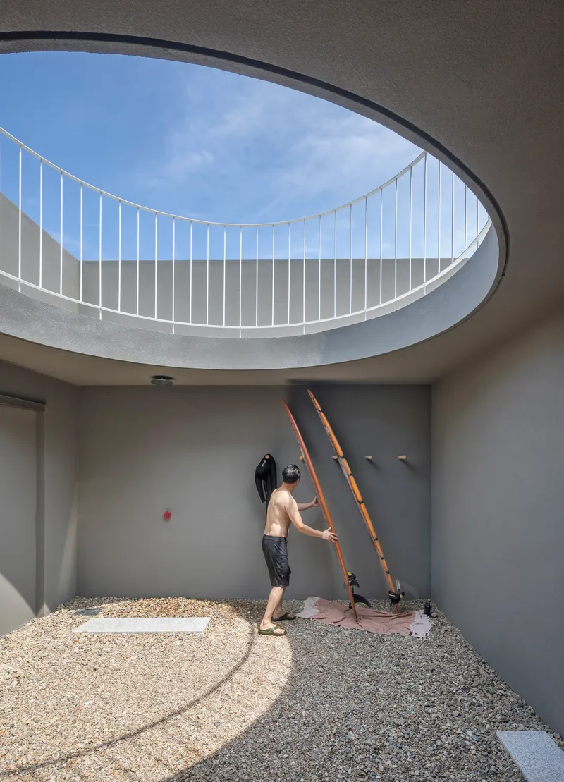 Person adjusting wooden ladder beneath circular skylight in gravel-floored courtyard