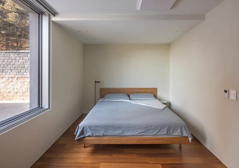 Bedroom with timber bed and wood floor beside full-height window overlooking stone retaining wall