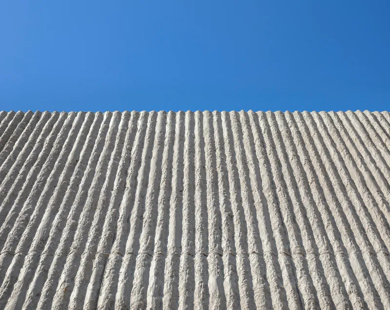 Upward view of ribbed concrete wall surface against a clear blue sky