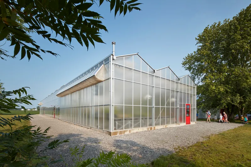 Corner view of the translucent polycarbonate facade with white structural framing and visitors on the gravel path