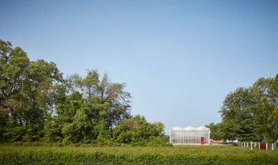 This image showcases a modern greenhouse set within a rural landscape. The greenhouse features a sym