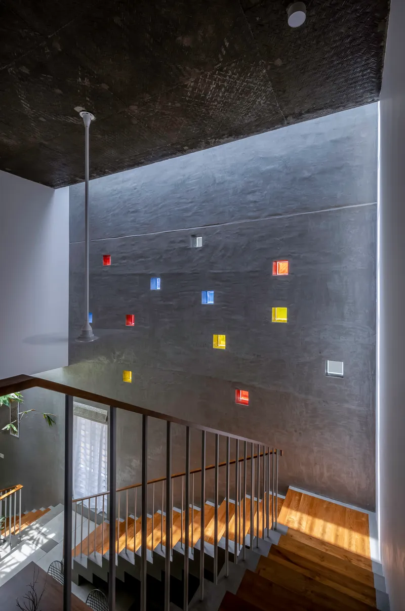Tall concrete wall with scattered colored glass block inserts beside a metal-railed staircase