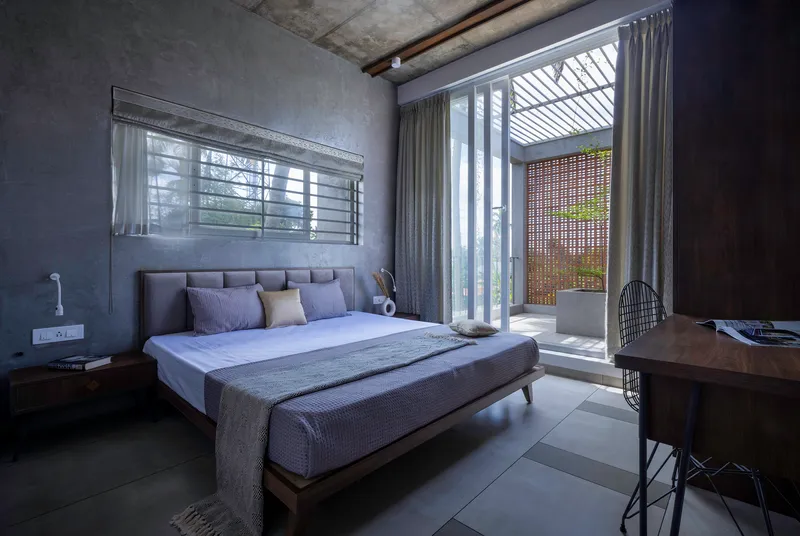 Bedroom with exposed concrete ceiling and view through curtained doors to a slatted terrace screen