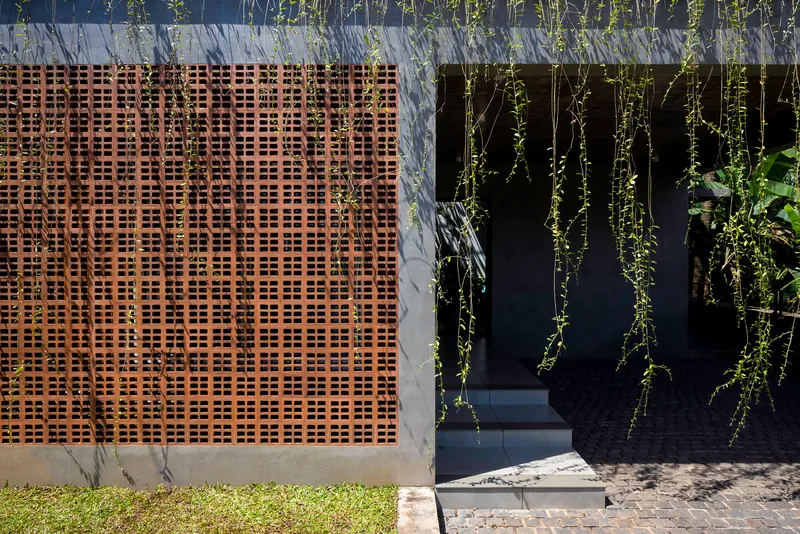 Perforated timber screen beside a dark entrance framed by cascading greenery and lawn edge