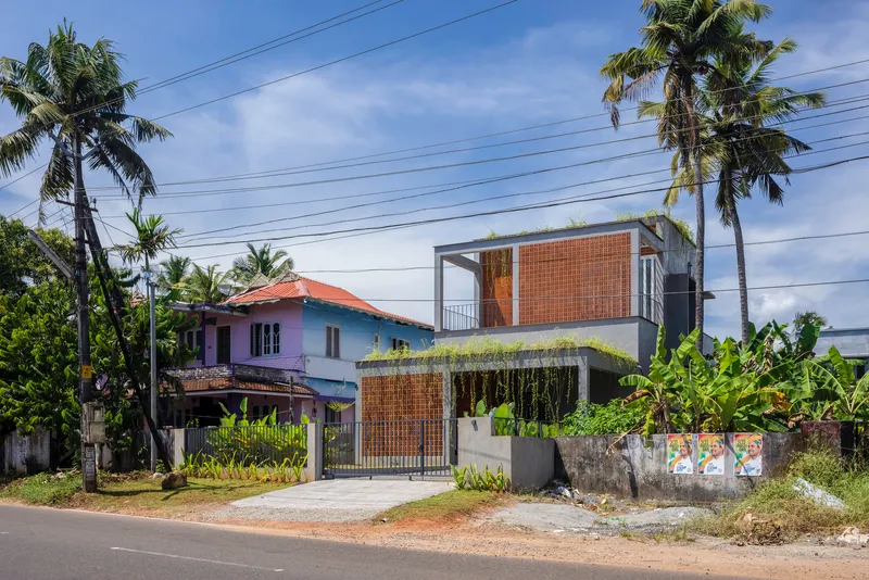 Two-story volume with bamboo screening and cascading greenery set behind a metal gate along a residential street