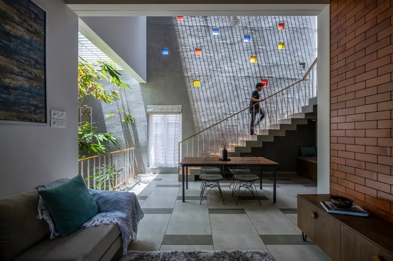 Double-height dining space with concrete stair and perforated brick wall filtering daylight from above