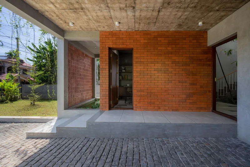 Covered entry terrace with exposed concrete ceiling, orange brick wall and planted courtyard beyond