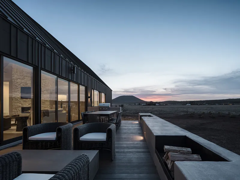 Timber deck terrace with wicker seating and fire pit facing distant hills at sunset