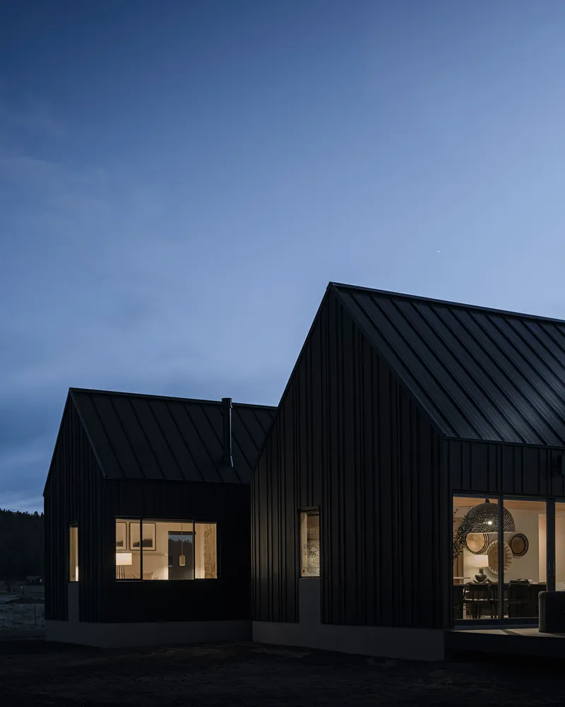 Adjoining gabled volumes with black metal cladding and lit windows under blue evening sky