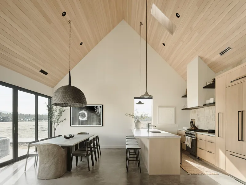 Kitchen and dining zone with pale wood island, vaulted wood ceiling and skylights casting daylight across concrete floors