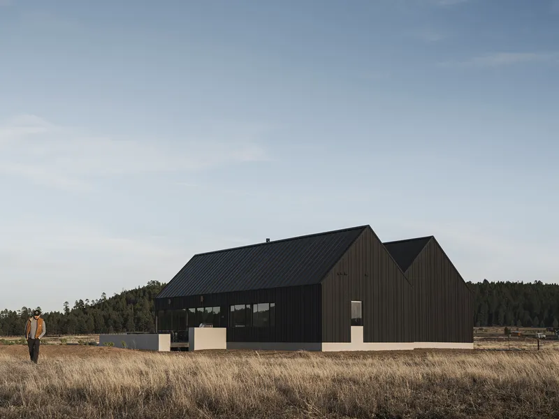 Black corrugated metal gabled volumes with a band of horizontal windows in dry grassland