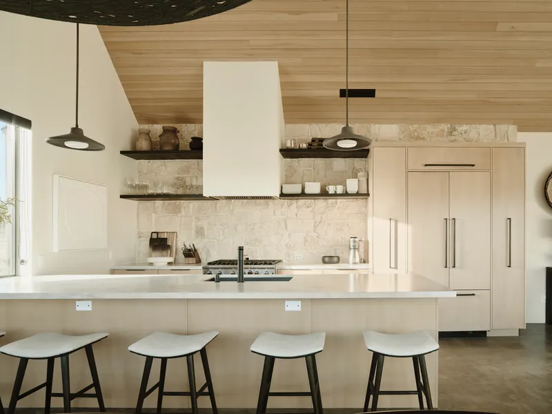 Kitchen island with four stools beneath a horizontal wood-clad ceiling and pendant lights