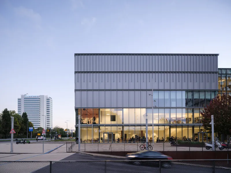 Corner view showing the ribbed facade and illuminated interior spaces at twilight
