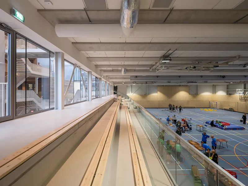 Sports hall with tiered wooden seating overlooking an active gymnasium floor