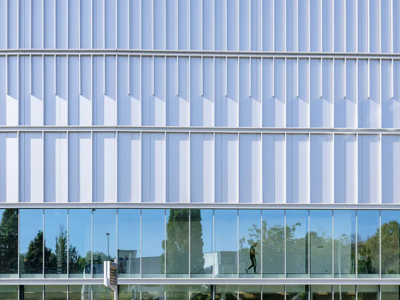 Close-up of vertical metal fins and glass curtain wall with a person walking inside