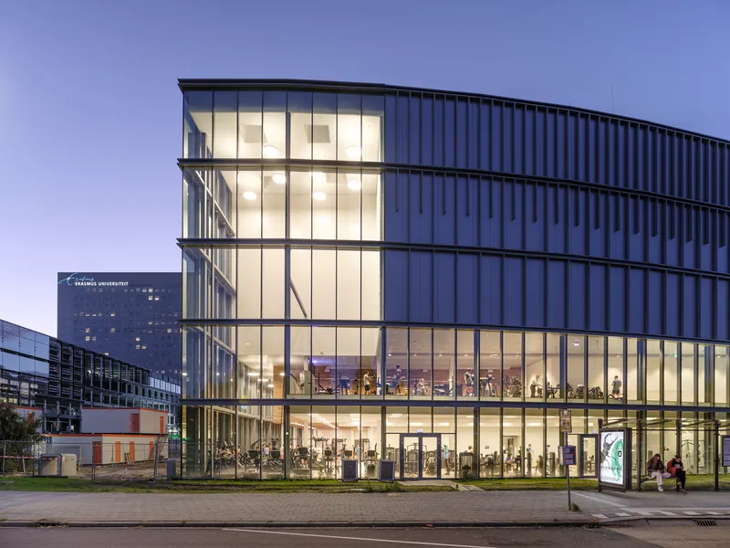 Five-story glass facade with vertical metal cladding above at twilight