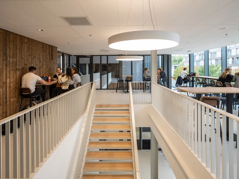 Open wooden staircase connecting split-level seating areas with vertical slat railings and pendant light