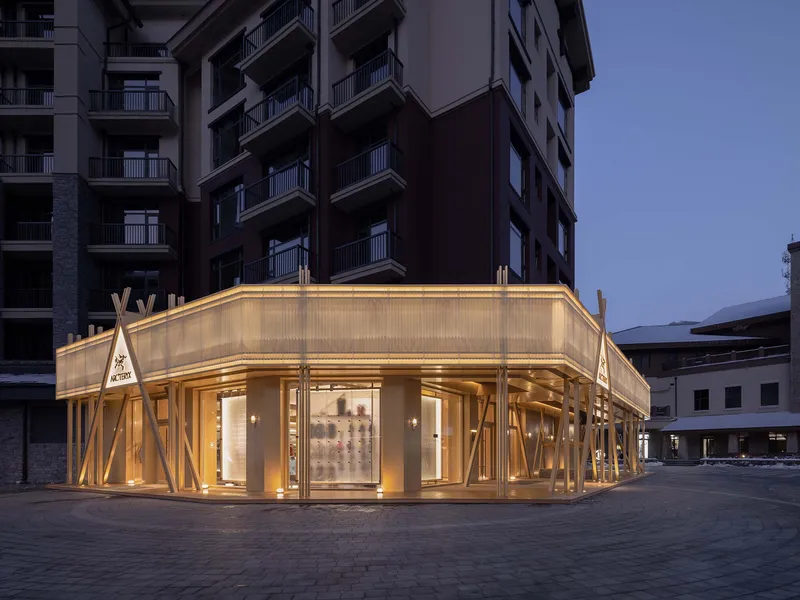 Illuminated corner storefront with diagonal timber columns and translucent panels at dusk