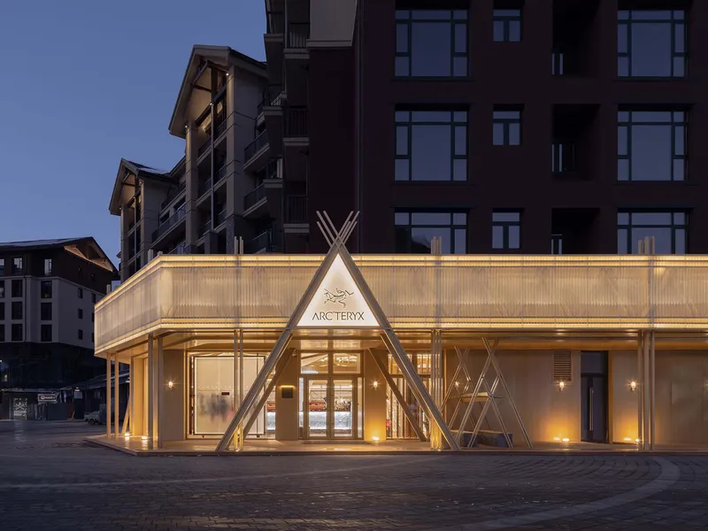 Illuminated translucent facade with triangular timber portal at street level during dusk