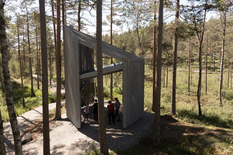 Open-air pavilion with vertical timber screens framing visitors seated beneath an angled roof plane